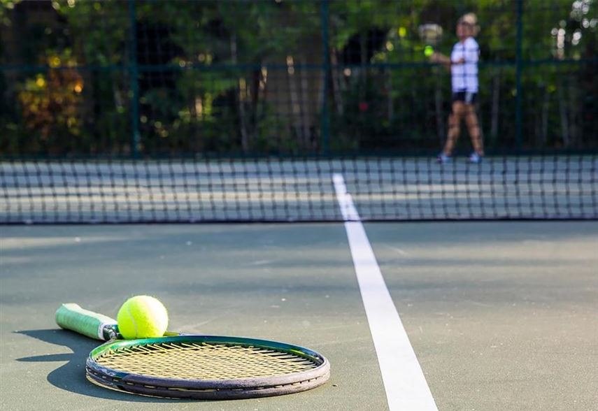 A racquet and ball on the court, with someone hitting at the far end