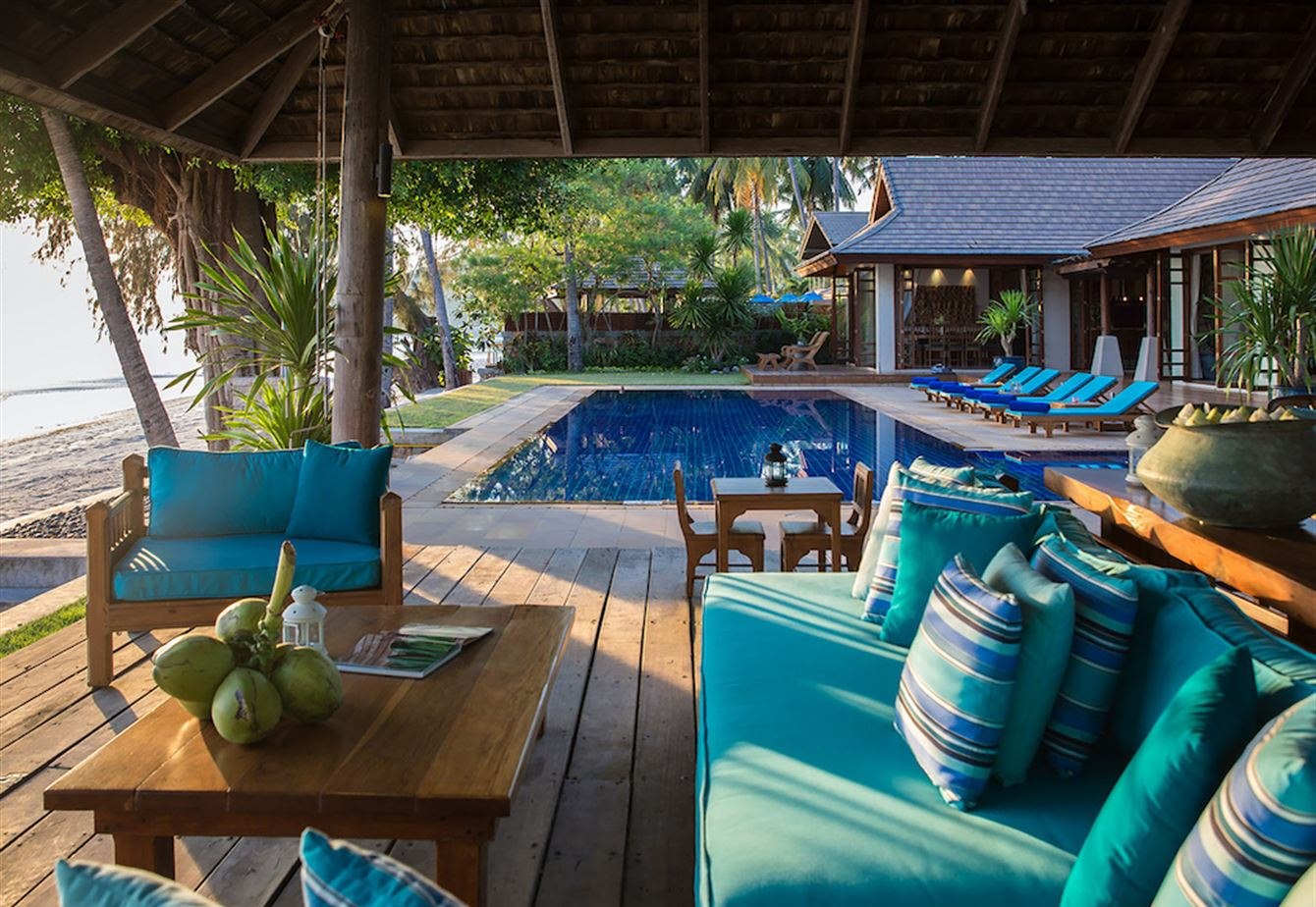 Cushioned daybeds under the beachside sala looking across the pool to the villa