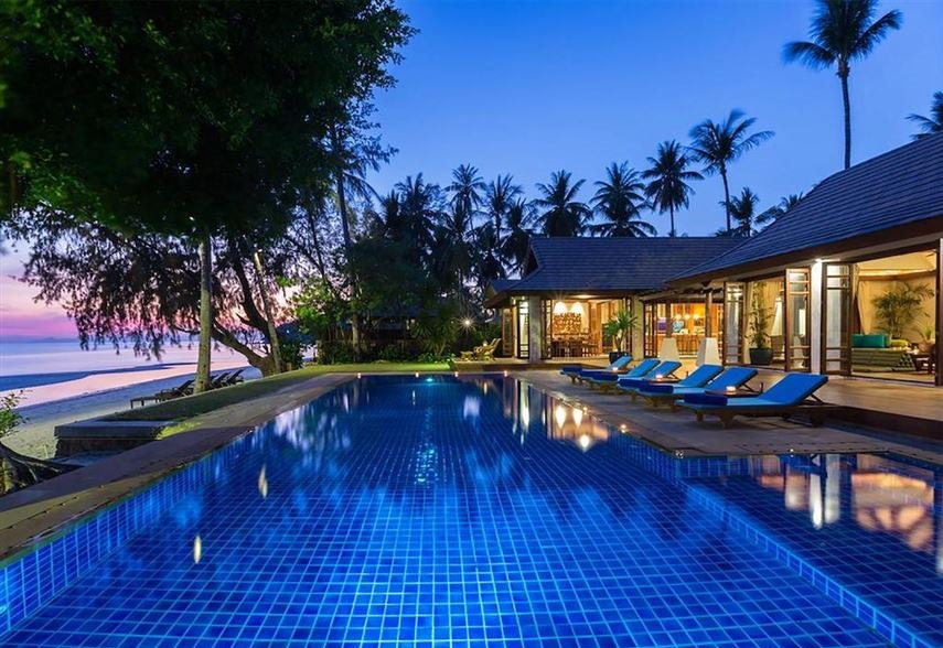 The villa's pool at dusk with the buildings lit and the sea beyond