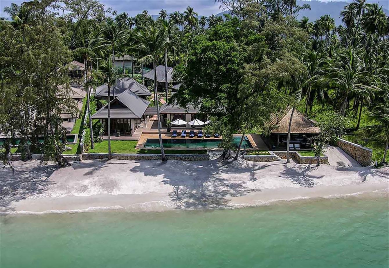The villa seen from the water, set among palms directly behind the sand