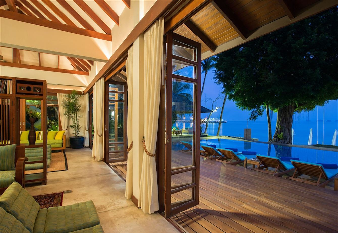 Living room doors folded open onto the deck, pool and sea at dusk
